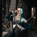 Fair skinned model wearing beaded black top and hand piece by Object & Dawn in a black silk dress standing in a dark, industrial setting